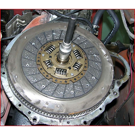 Nahaufnahme einer Kupplungsscheibe mit Werkzeug. Die Scheibe ist grau, mit metallischen Federn und einem Führungsstift.